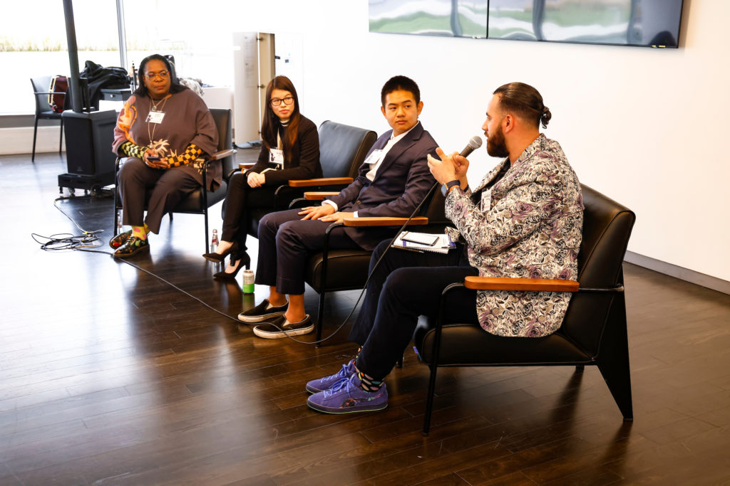 Image from Building Hope Mental Health Strategy Summit, hosted by Inseparable on November 16, 2022. 2 male and 2 female panelists, Keris Jän Myrick and Kenna Chic, sitting in chairs at the front of a room. One man with a mic is speaking.