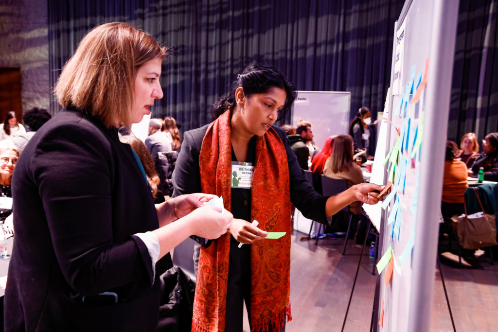 Image from Building Hope Mental Health Strategy Summit, hosted by Inseparable on November 16, 2022. Krithika Harish and another women are working on a whiteboard with post its.