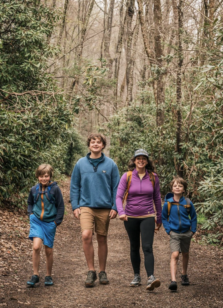 A woman and three boys hike along a forest trail.