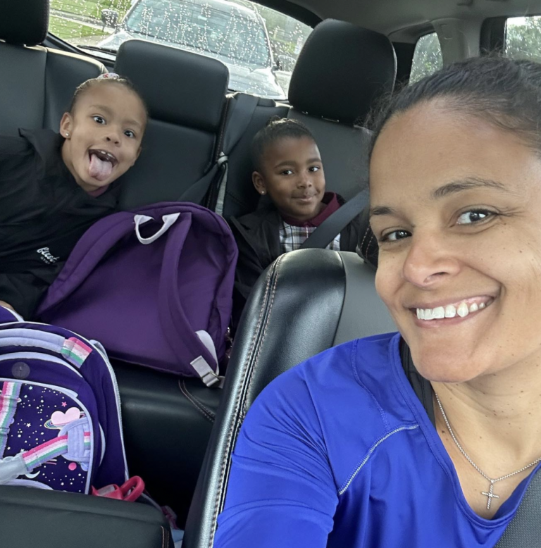 Woman taking a selfie with two daughters inside a car.
