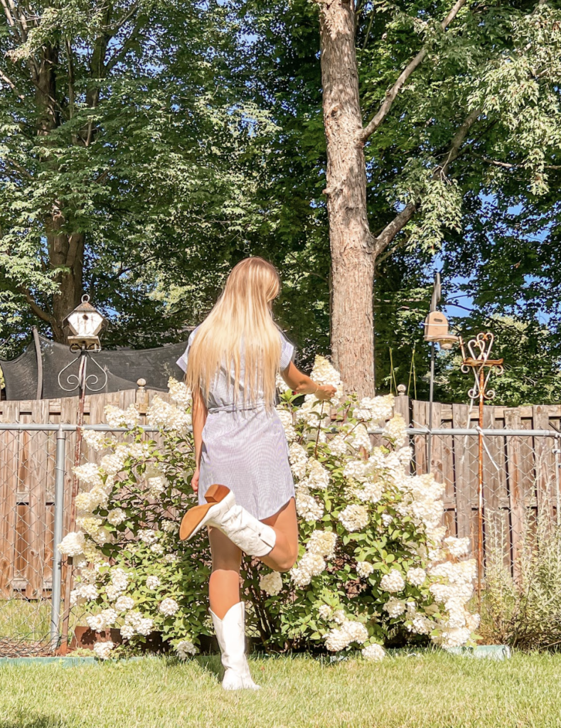 A young woman stands in front of a garden.