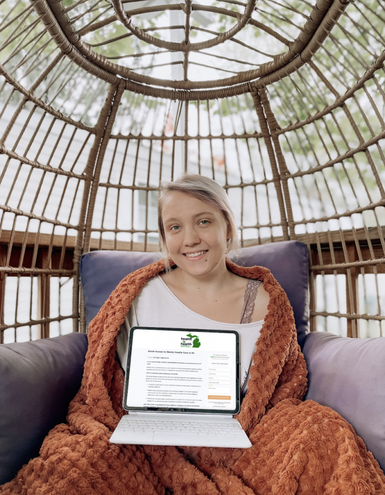 A woman sits in a swinging tree holding a laptop open on a mental health care petition.