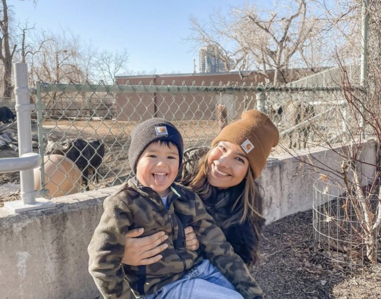 A woman holds a young boy from behind and smiles at the camera.