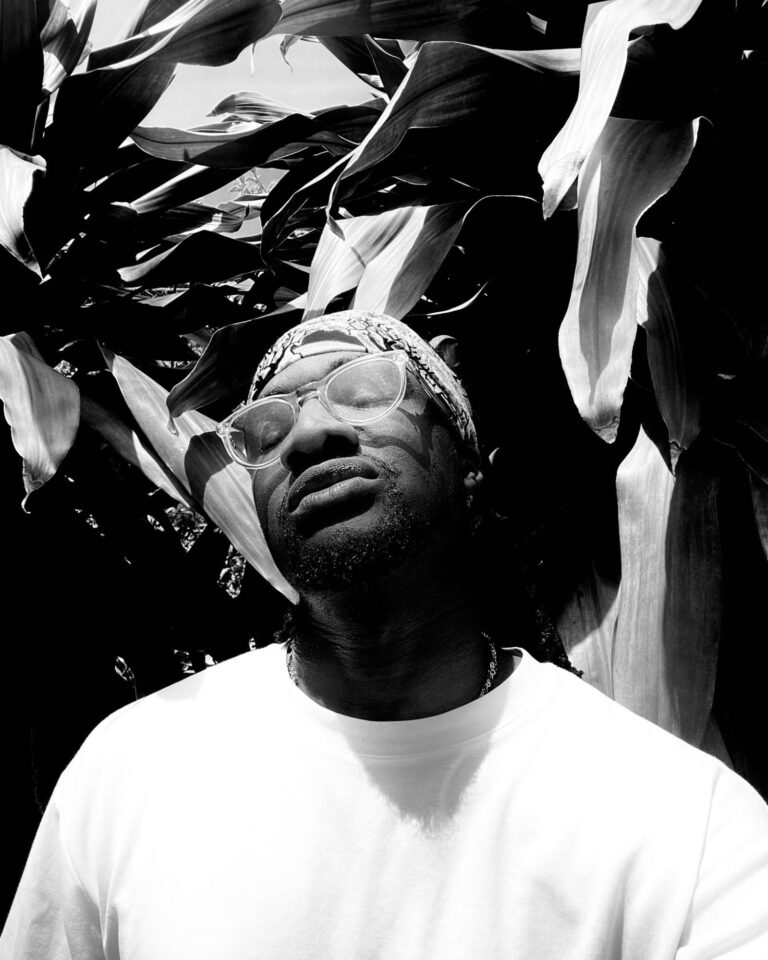 A man stands in front of lush plants with his eyes closed.